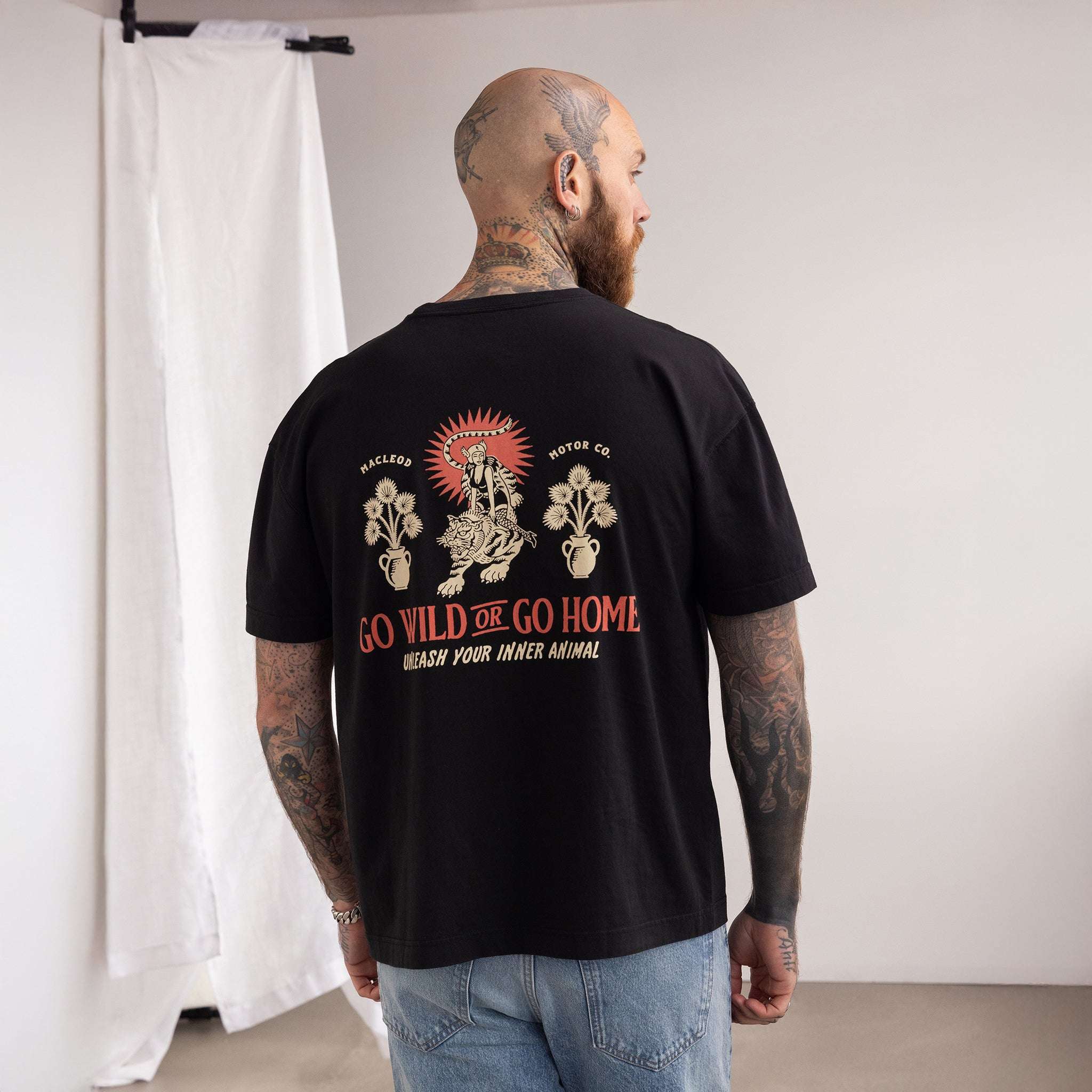 Man wearing a black t-shirt with a graphic design on the back, standing against a plain wall.