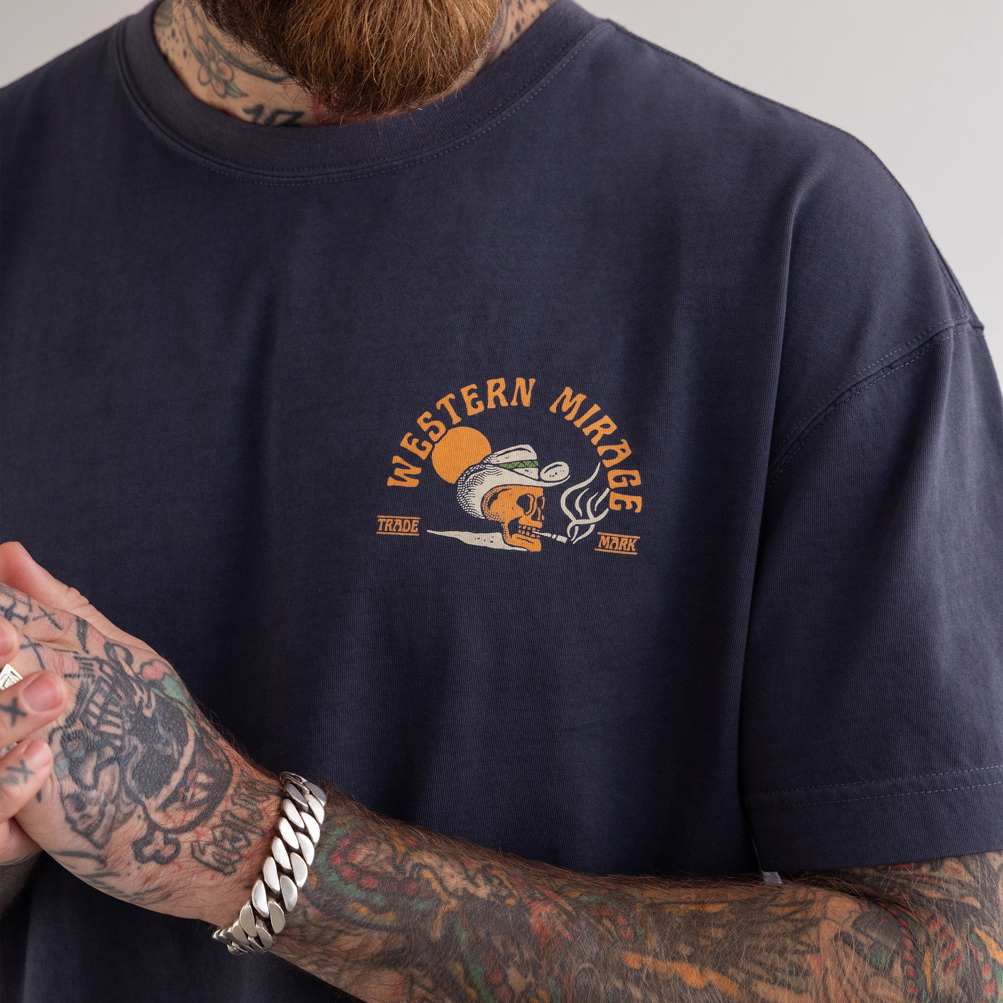 Navy blue t-shirt with 'Western Mirage' logo worn by a person with tattoos.