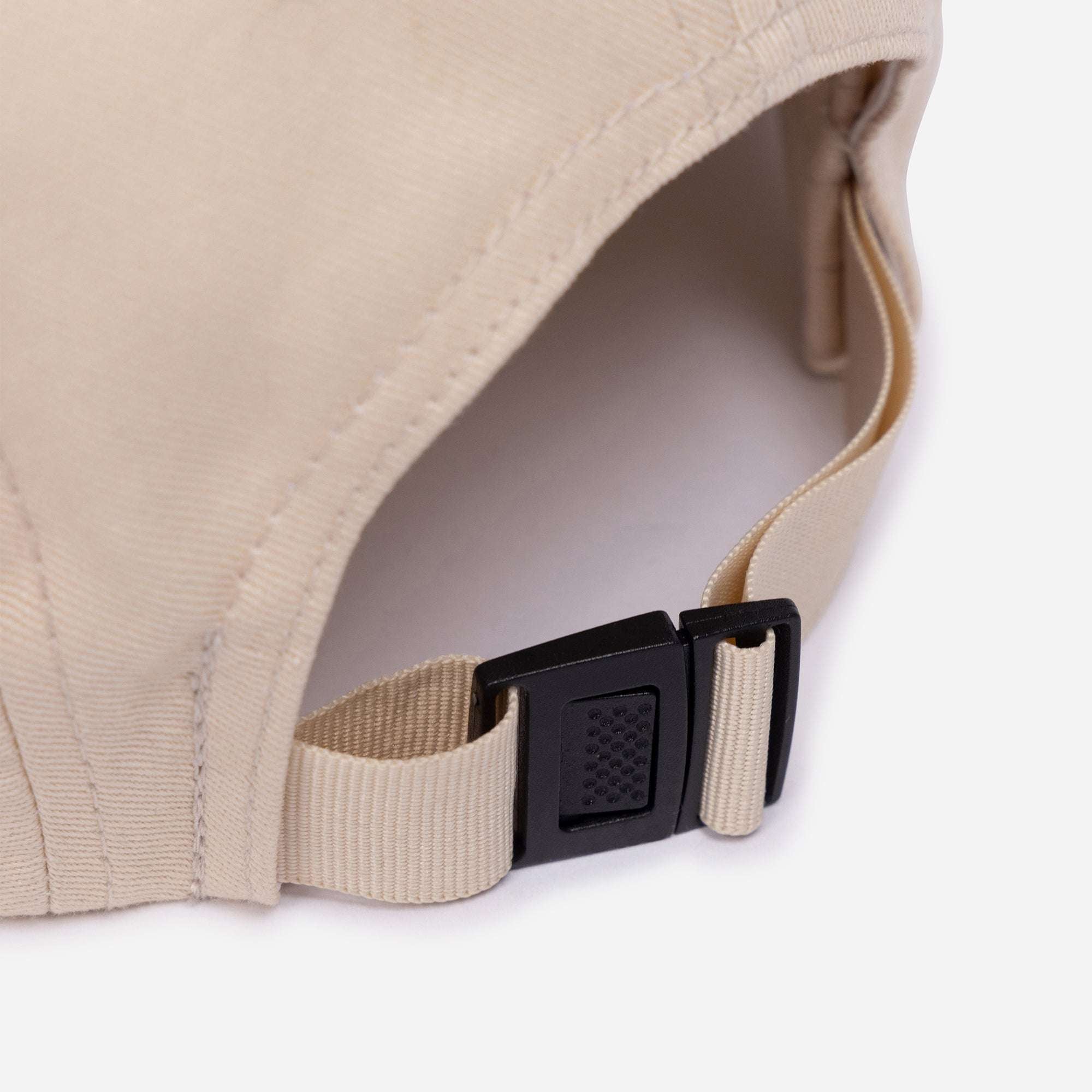 Beige cap with a black adjustable strap on a white background