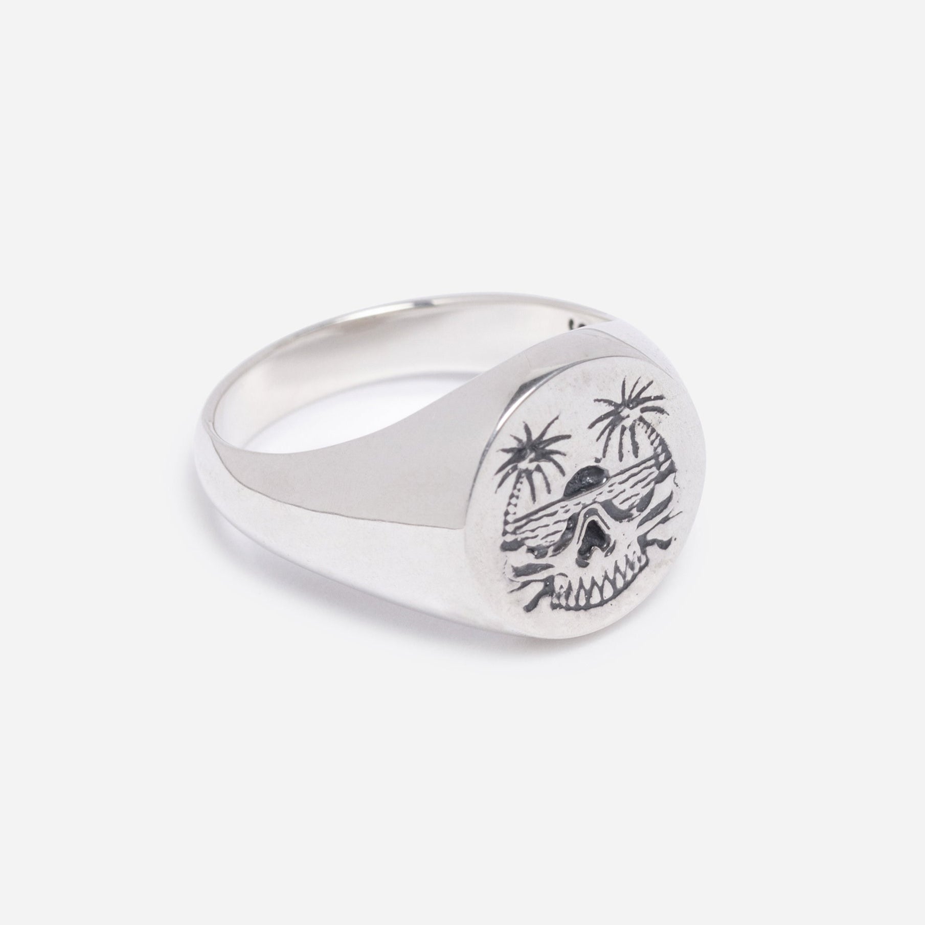Silver ring with a skull and palm tree design on a light gray background