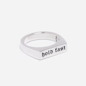 Silver ring with 'hold fast' engraving on a light gray background