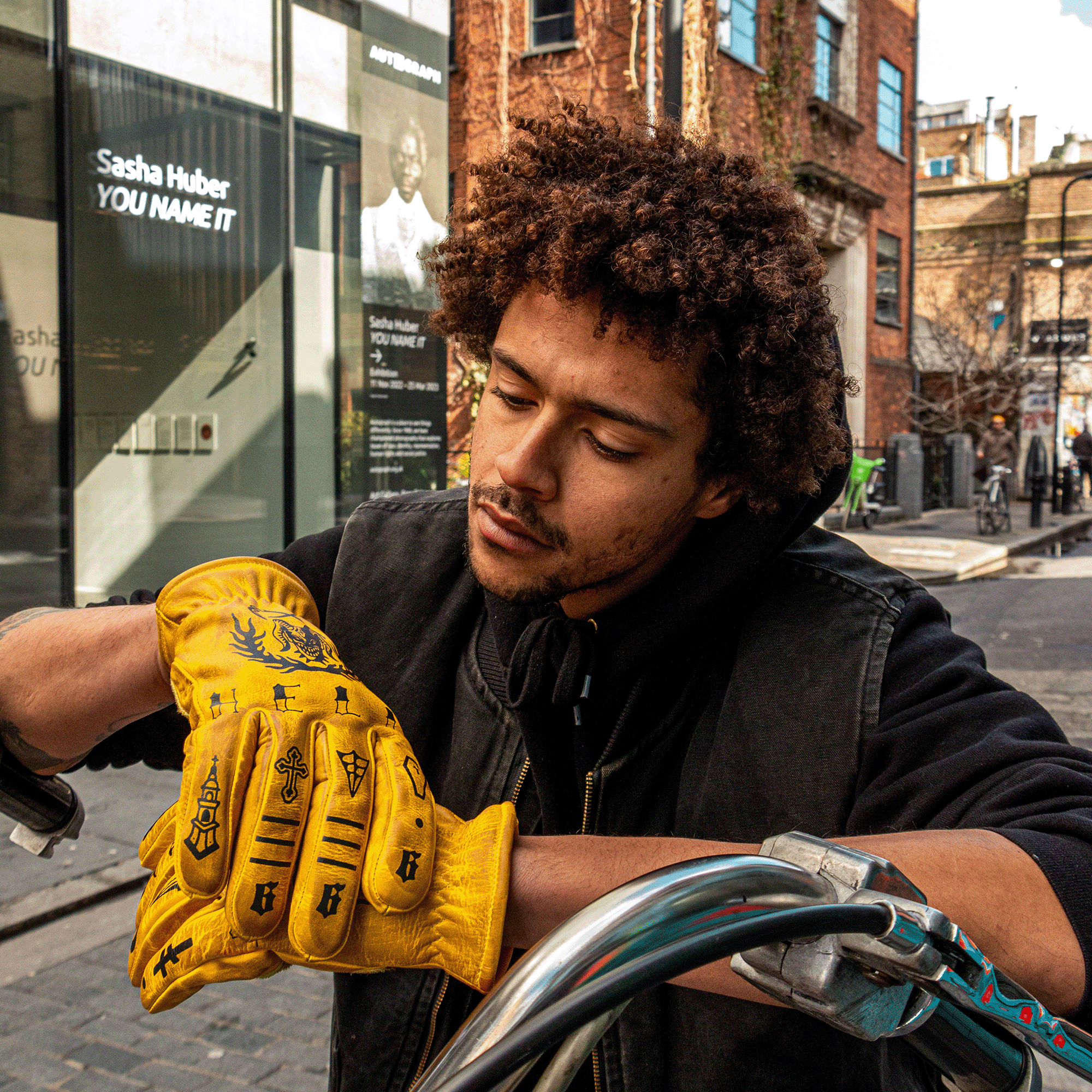 Person wearing yellow motorcycle gloves and a black jacket on a city street